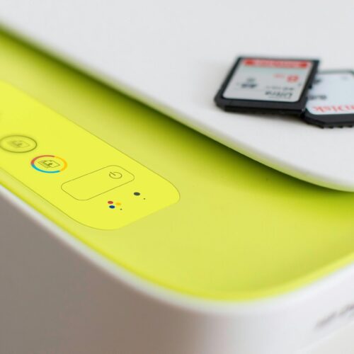 A close-up of a yellow and white printer with control buttons on the top. Two SD cards, one labeled Sandisk, are placed on the upper right corner of the printer.