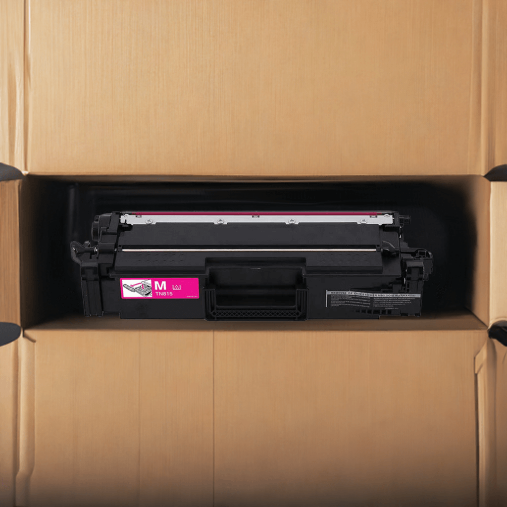 A magenta printer toner cartridge labeled M inside an open cardboard box, viewed from above.