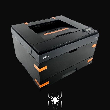 A black refurbished Dell printer with orange tape on the edges sits on a dark surface, with a white spider symbol beneath it.